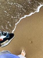 Barefoot walk on sandy beach with waves and sneakers photo