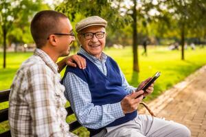 Portrait of happy grandfather and grandson in park. They are spending time together and using digital tablet. photo
