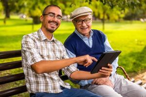 Portrait of happy grandfather and grandson in park. They are spending time together and using digital tablet. photo
