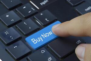 Finger presses blue Buy Now key, highlighting simple e commerce interaction photo