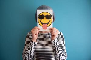 Card with smiley face hides persons face, playful tone against blue background photo