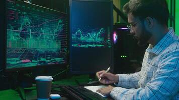 Arabian Indian man programmer coder writing notes analyst guy screen finish computer IT technology work complete database male trader freelancer crypto currency hacking night office pc stretch hands video