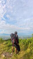 Hiker with backpack standing on top of the mountain and looking at the view. photo