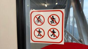 Sign on glass with 4 symbols prohibiting use of personal transport when entering public place, ban on use of bicycle, scooter, skateboard and roller skates with special sign for safety reason photo