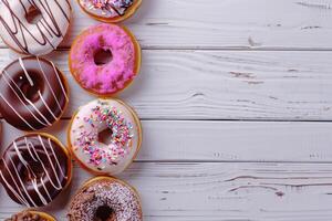 Copy space image of delicious donuts drizzled with icing and chocolate presented on a white wooden background photo