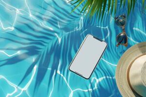 Mobile phone mockup with blank screen laying on the blue water of the sea or pool with palm tree, sunglasses and hat photo