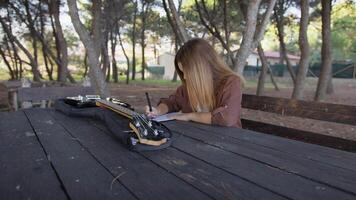Girl Writes Music Notes On Sheet Music Sitting At The Park Table In The Nature video