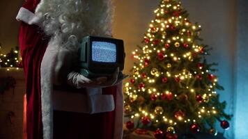 Santa Claus Holds A Vintage Television With Static Signal In Front Of Tree video