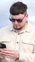 young caucasian man sitting on a bench in the park and using smartphone, writing messages video