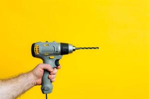 Man's hand holds a cordless drill on a yellow background, space text photo