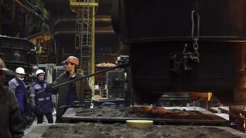 Workers are actively engaged in the metal casting process within a busy manufacturing environment. Stock Clip photo