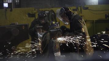Workers are actively engaged in welding and grinding tasks within an industrial workshop. Stock Clip photo