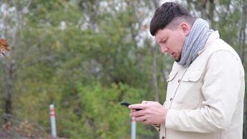 young caucasian man sitting on a bench in the park and using smartphone, writing messages video