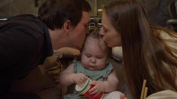 Mother and father are kissing their child on both sides, while the daughter is excitedly playing with colorful cups, preparing for her upcoming birthday. video