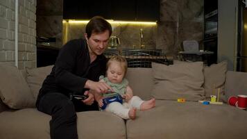 A young child is trying to play a game using a controller while sitting in the living room with their father. video