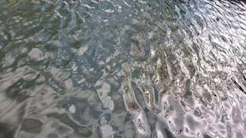 Wavy green water surface with bokeh of sun glares moving in slow motion. Rippled water texture with blurry reflection in bright sunlight. Calm smooth liquid background video