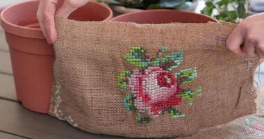 Creating a beautiful garden display flower pots using burlap embroidered with cross-stitch motif rose . This process showcases how to add a personal touch with decorative materials and plants. video