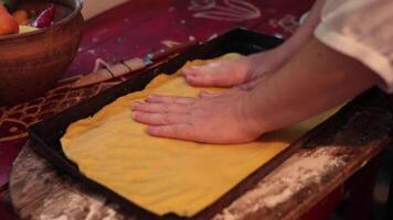 POV hands press kneaded and rolled dough over surface of baking tray closeup. Kitchen cutting board with flour, cookware, ingredients on rustic table. Baking, cooking process, recipe of apple pie video