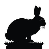 A black and white silhouette of a rabbit sitting on grass vector