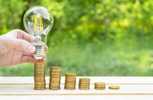 Business concept. A hand holds a lamp over coins on a wooden table with a green bokeh background. New ideas and creativity. Business ideas, business success. Recovery and business growth. Copy space. photo