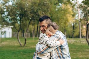 Portrait of positive, smiling father and cute little boy embracing together, in the forest photo