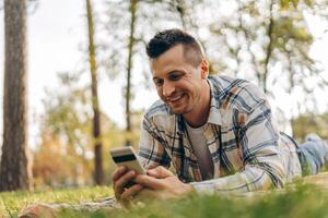 Portrait of happy man lying on blanket holding mobile phone using mobile app watching outdoors photo