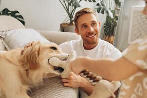 Smiling, attractive man, father playing with dog, golden retriever, sitting on comfortable sofa photo