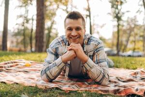 Smiling, handsome middle aged man lying on blanket on green grass in forest looking at camera photo