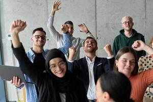 A diverse team of business professionals ecstatically celebrating their success in a modern office, expressing triumph and unity after achieving their goals photo