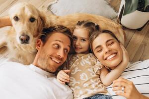 Smiling family and golden retriever hugging together, lying, embracing in cozy living room at home photo
