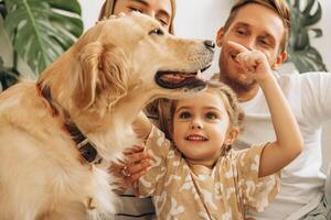 Happy, beautiful mother, father, cute little daughter playing together with dog, golden retriever photo