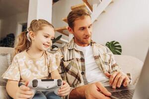 Handsome father and little daughter together sitting on comfortable sofa, holding joystick photo