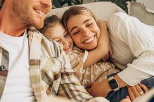 Smiling happy family smiling mother father hugging with little daughter, sitting on comfortable sofa photo