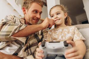 Smiling, excited man, little daughter and father playing together game, holding console photo