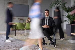 A businessman in a wheelchair navigating through a busy office, surrounded by his colleagues who are actively engaged in their work and collaboration photo