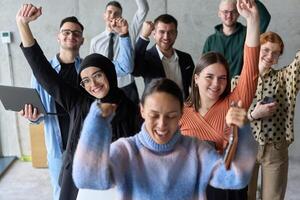 A diverse team of business professionals ecstatically celebrating their success in a modern office, expressing triumph and unity after achieving their goals photo