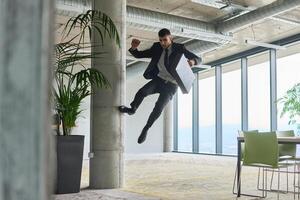 A businessman ecstatically jumping in a modern office, holding a briefcase in his hands, celebrating a moment of success and triumph. photo