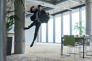 A businessman ecstatically jumping in a modern office, holding a briefcase in his hands, celebrating a moment of success and triumph. photo