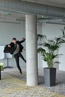 A businessman ecstatically jumping in a modern office, holding a briefcase in his hands, celebrating a moment of success and triumph. photo