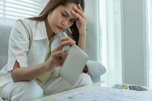 Stressed and headache asian woman with large bills or invoices no money to pay to expenses and credit card debt. shortage, Financial problems, mortgage, loan, bankruptcy, bankrupt, poor, empty wallet photo