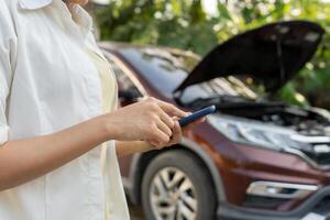 breakdown, broken car, repair. Woman uses mobile phone check insurance premiums through application due to car accident . Find garage to get car fixed during country tour, waiting for help, emergency. photo