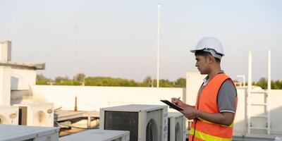 Asian maintenance engineer works on the roof of factory. contractor inspect compressor system and plans installation of air condition systems in construction. Checklist, inspector, control photo