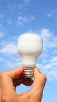 A person holding a light bulb in front of a blue sky photo