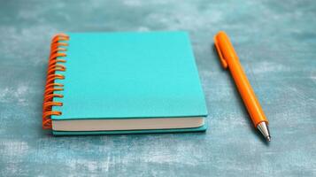 Turquoise notebook with orange pen on textured surface. photo
