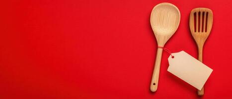 Wooden cooking utensils with a blank tag on a vibrant red background. photo