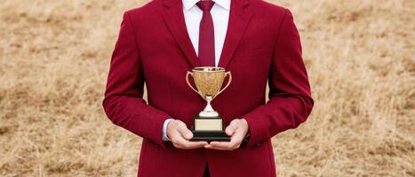 A man in a red suit holding a trophy against a natural background of dry grass. photo