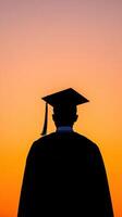 Silhouette of a graduate wearing a cap against a vibrant sunset sky. photo