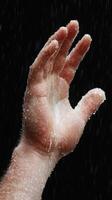 A hand reaching out, illuminated by droplets of water in a dramatic atmosphere. photo