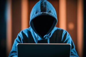 A mysterious figure in a hoodie using a laptop in low light, representing cyber anonymity. photo