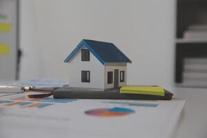 Wooden table with laptop, house keys Clipboard with pen, house model and green tree calculator, real estate concept. close up pictures photo